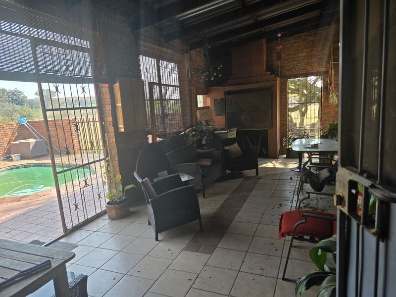 Covered patio area featuring a built-in braai, exposed brick walls, and tiled flooring, with direct access to the pool area.