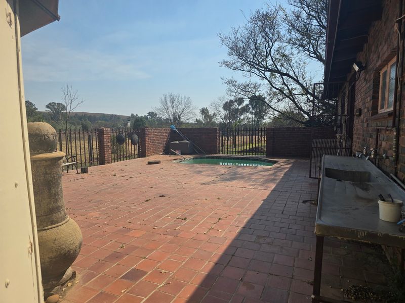 Outdoor patio area featuring a swimming pool, brick paving, and a built-in outdoor sink, set against a rural landscape.