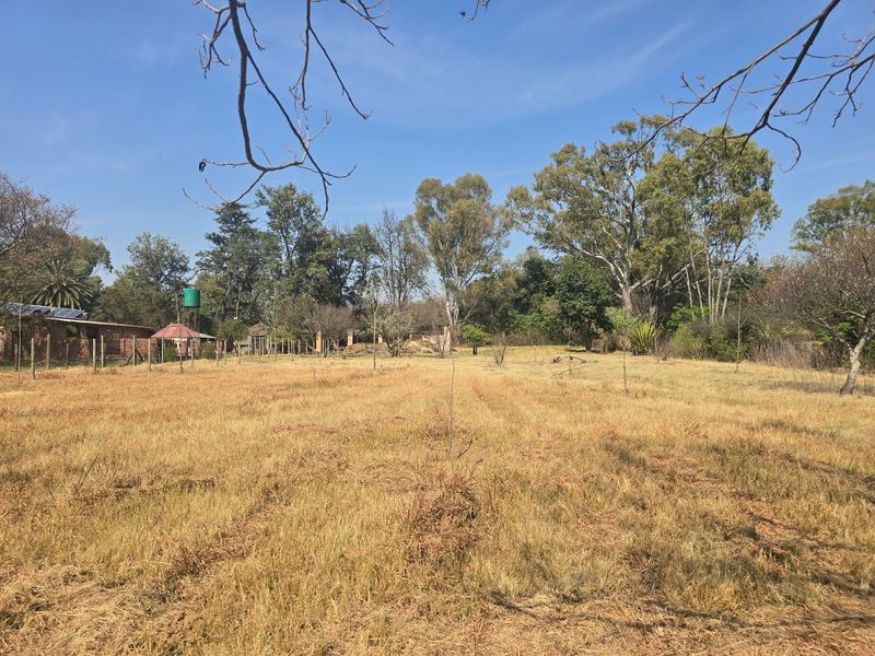 Expansive open farm land featuring mature trees, perimeter fencing, and a water tank, offering a peaceful rural landscape.