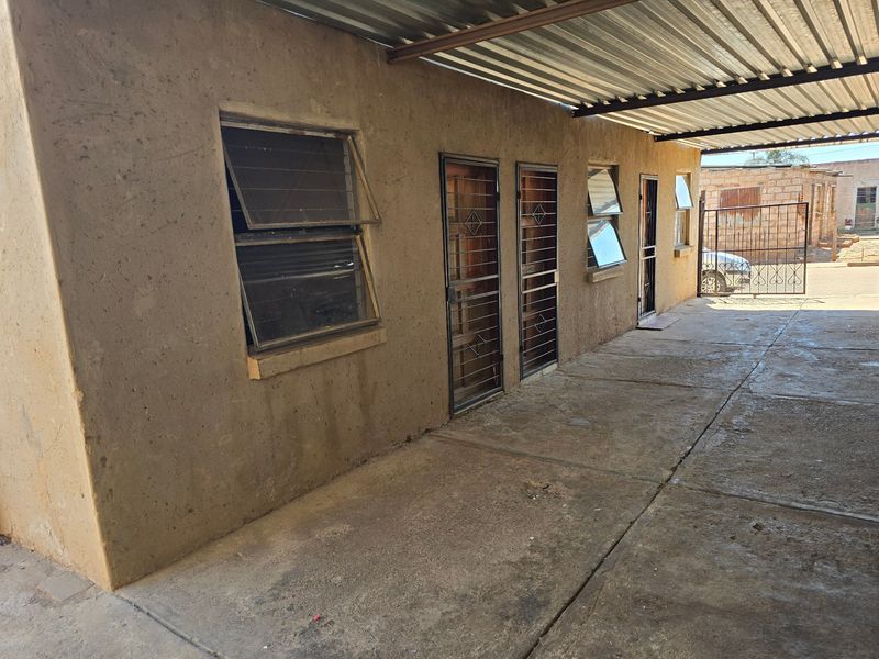 Exterior view of a property featuring a corrugated metal roof, concrete driveway, and multiple security-gated entrances with louvre windows.