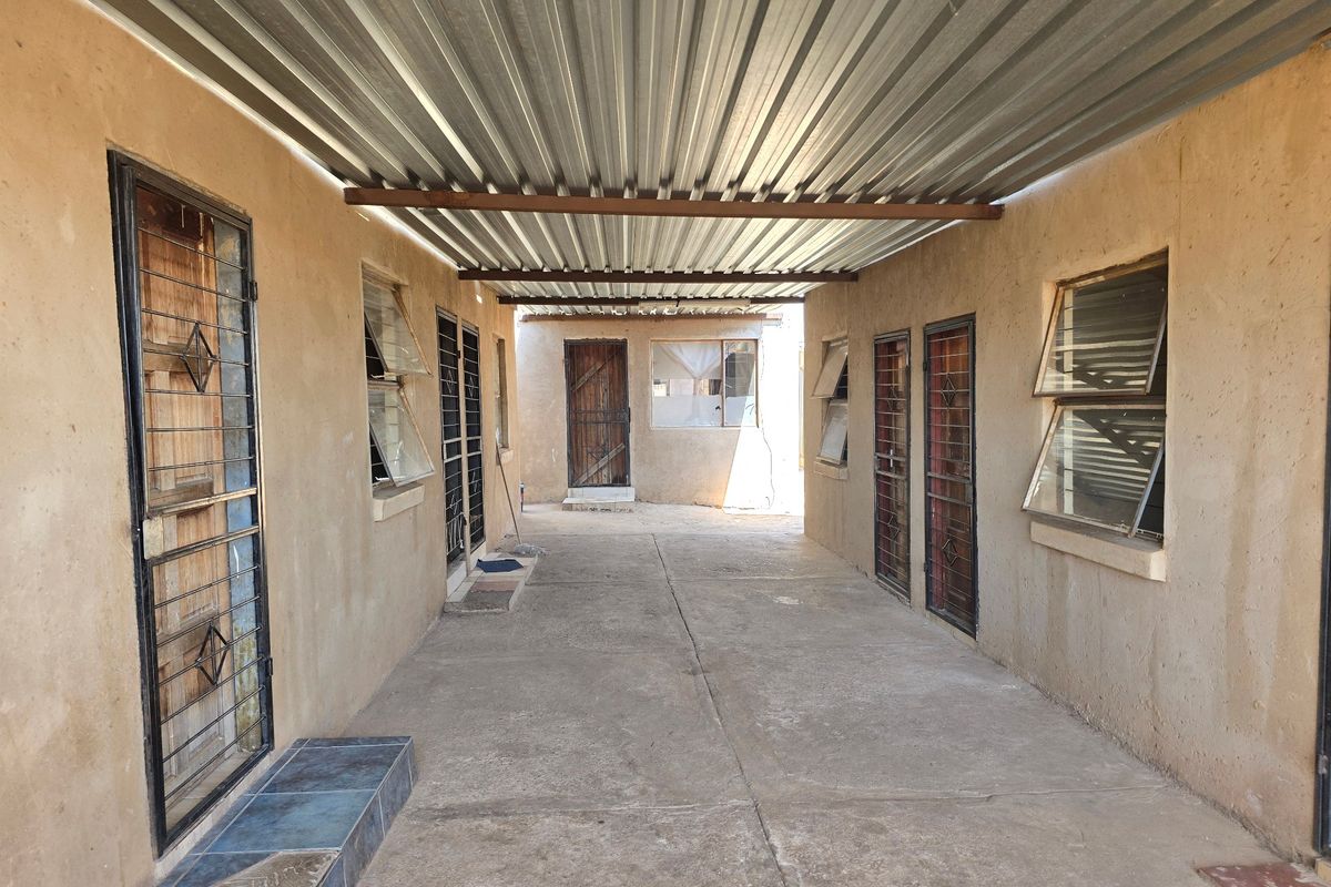 A covered outdoor walkway or courtyard area featuring corrugated metal roofing, security gates, and multiple access points to the property.