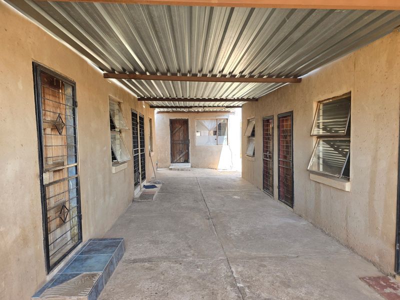 A covered outdoor walkway or courtyard area featuring corrugated metal roofing, security gates, and multiple access points to the property.