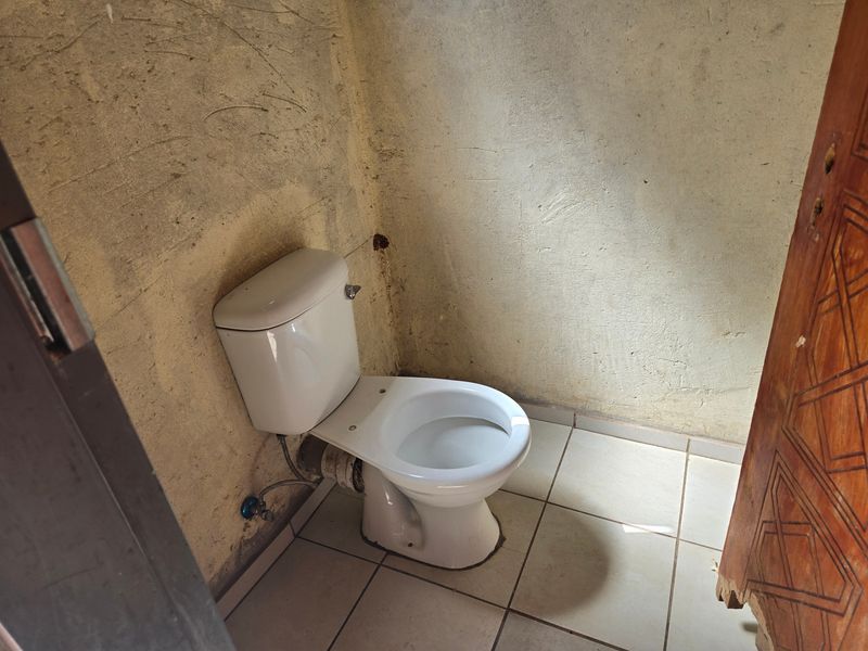 A small bathroom featuring a white toilet and tiled flooring, currently requiring significant wall finishing and general renovation to improve the space.
