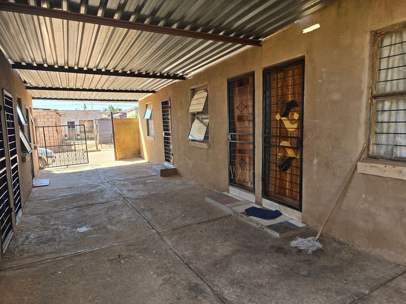A covered outdoor patio area featuring a corrugated metal roof, concrete flooring, and multiple access points with security gates and bars.