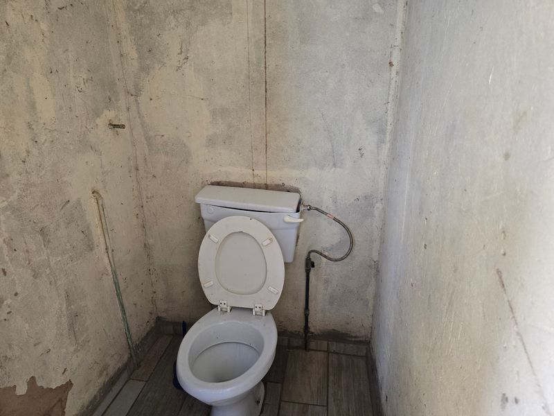 A small bathroom space featuring a toilet, requiring significant wall repairs and finishing to restore functionality and aesthetic appeal.