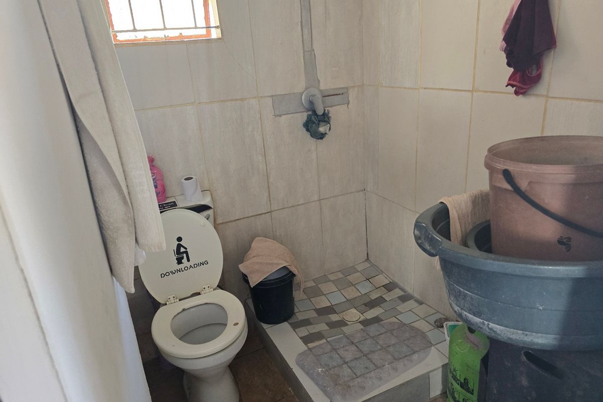 A small bathroom featuring a toilet and a tiled shower area with exposed plumbing and dated wall finishes.