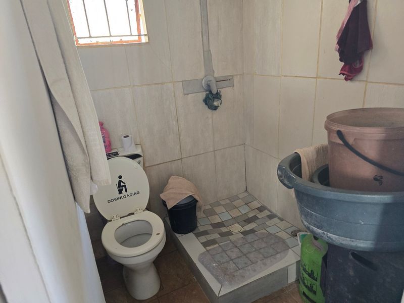 A small bathroom featuring a toilet and a tiled shower area with exposed plumbing and dated wall finishes.