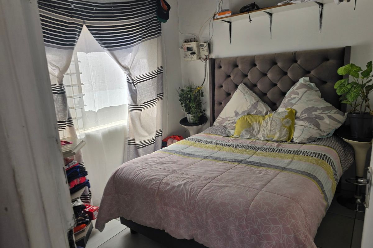 A compact bedroom featuring tiled flooring, wall-mounted shelving, and an exposed electrical distribution board.