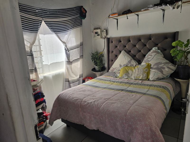 A compact bedroom featuring tiled flooring, wall-mounted shelving, and an exposed electrical distribution board.