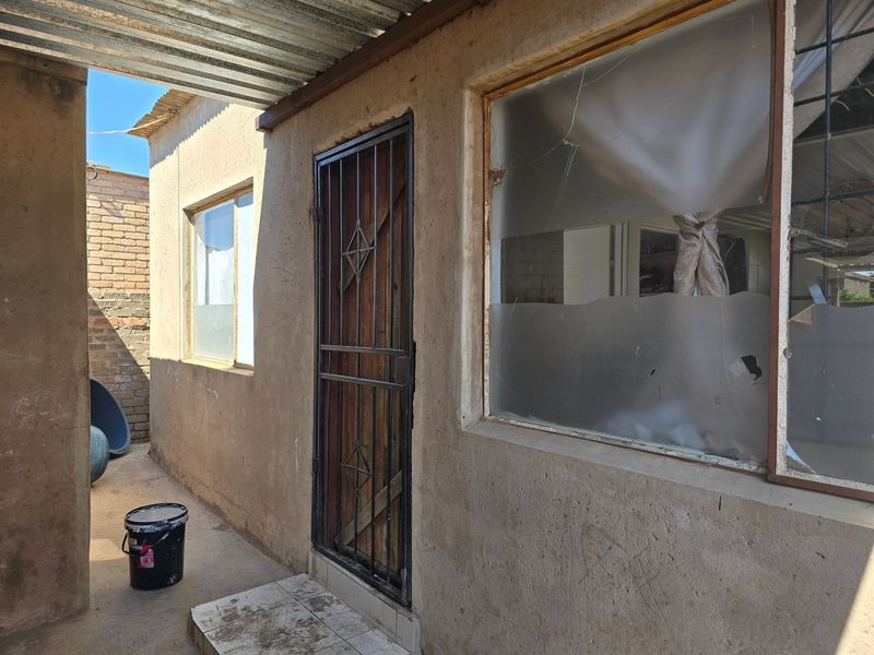Rear exterior view of the property featuring a security gate, corrugated roofing, and a damaged window pane requiring repair.