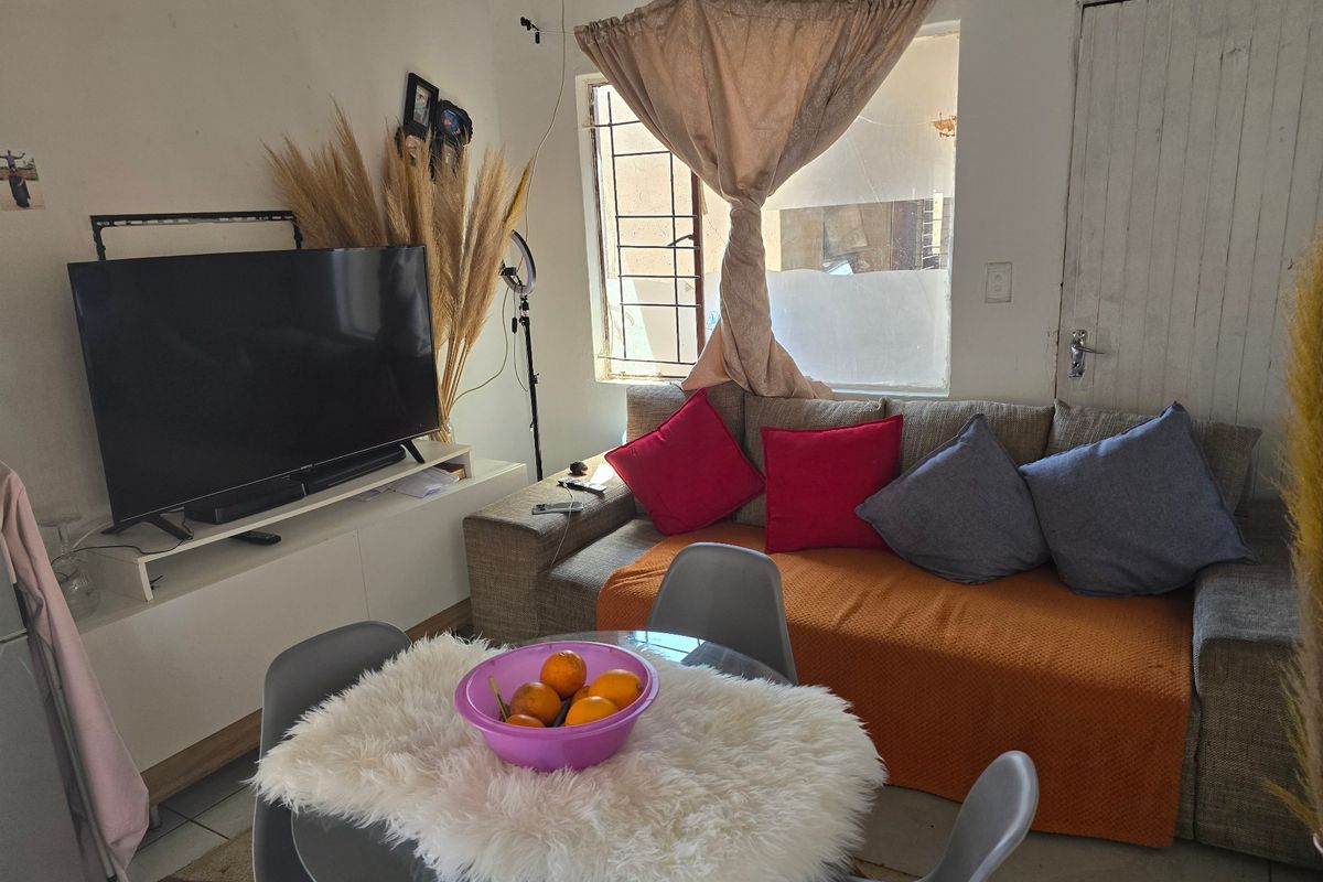 A compact living area featuring tiled flooring and a window fitted with security bars, offering a functional space for relaxation.