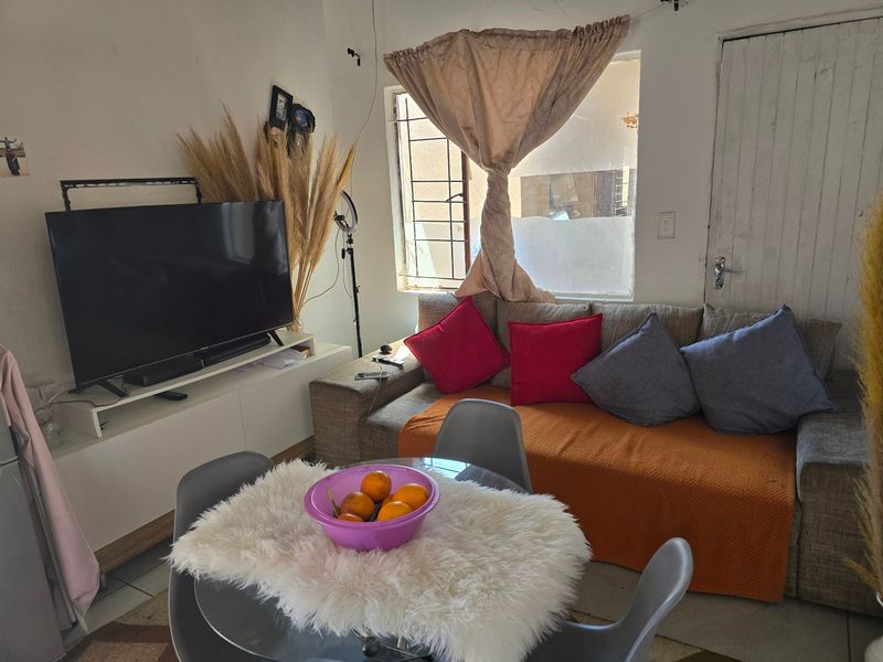 A compact living area featuring tiled flooring and a window fitted with security bars, offering a functional space for relaxation.