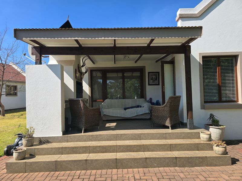 A covered patio area featuring tiled steps, a timber pergola structure, and a built-in fireplace, providing a functional outdoor entertainment space.