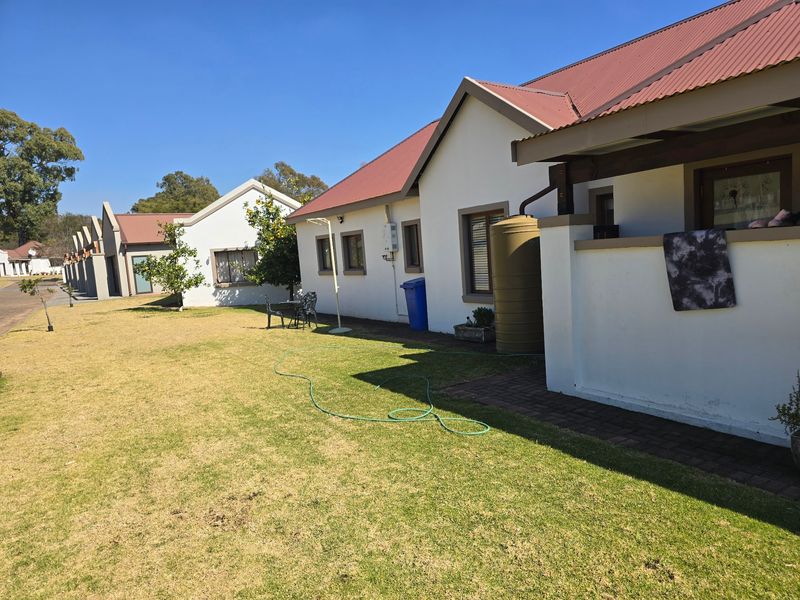 Rear view of a townhouse featuring a corrugated metal roof, a water tank, and a well-maintained lawn area.