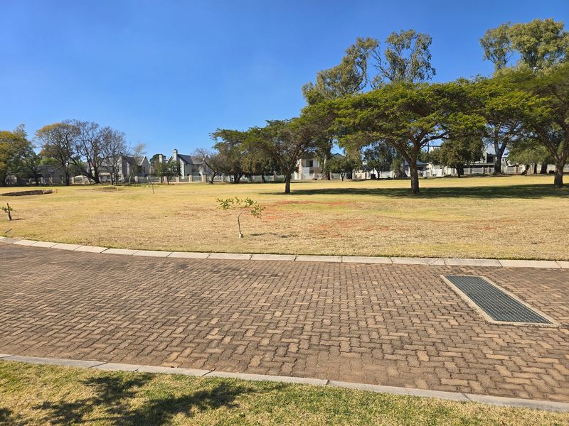 A view of a spacious communal lawn area with mature trees and a paved driveway in the foreground.