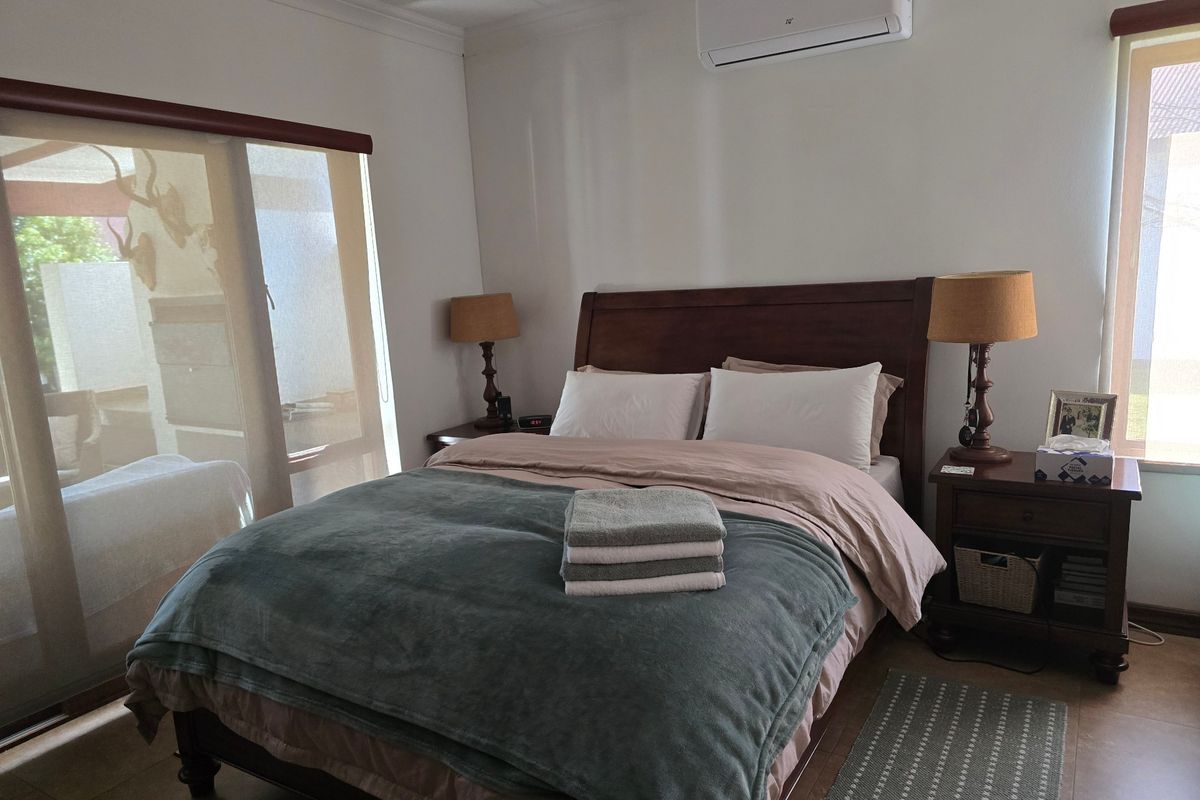 A well-maintained bedroom featuring tiled flooring, a wall-mounted split-system air conditioner, and large windows with roller blinds for natural light control.