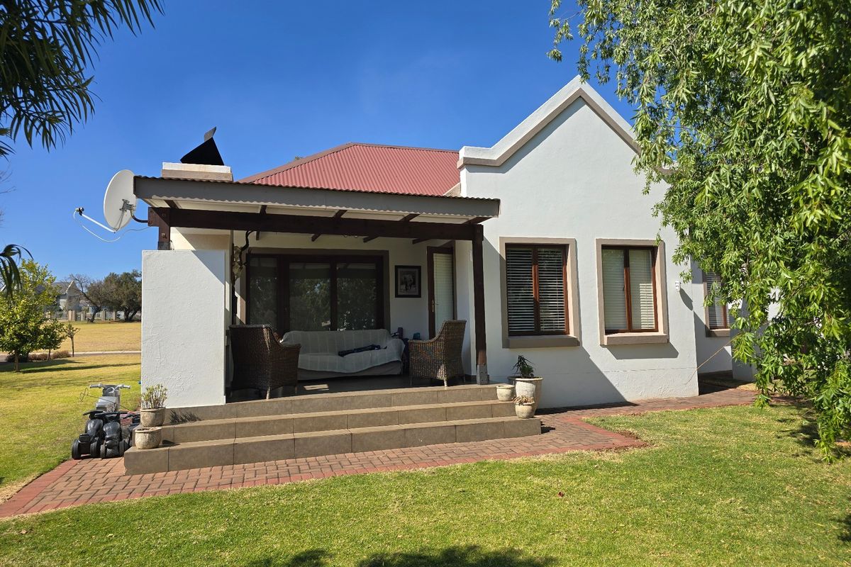 Rear view of the townhouse featuring a covered patio with tiled steps, brick paving, and a well-maintained garden area.