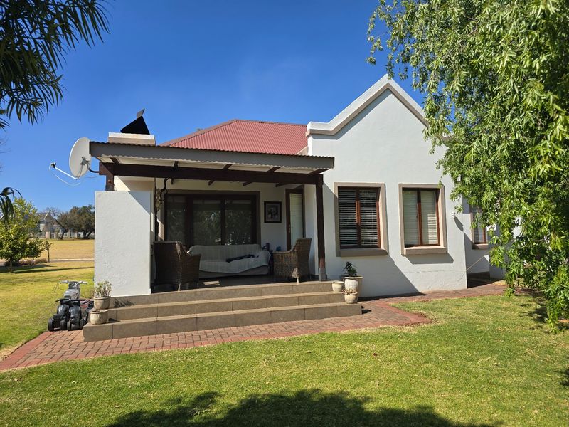 Rear view of the townhouse featuring a covered patio with tiled steps, brick paving, and a well-maintained garden area.