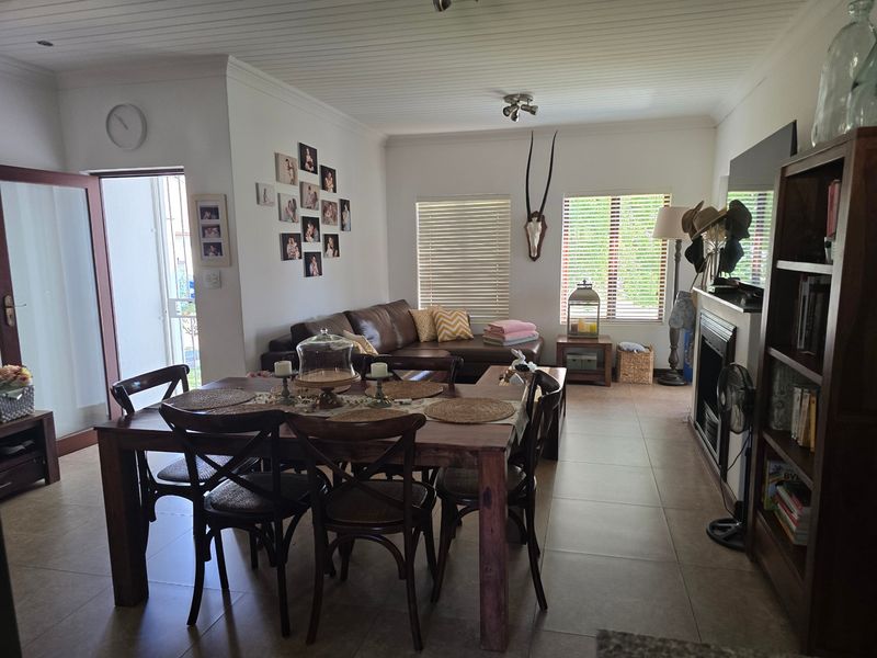 An open-plan living and dining area featuring tiled flooring, a built-in fireplace, and a tongue and groove ceiling with recessed lighting.
