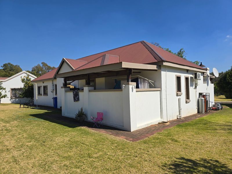 Rear view of the townhouse featuring a covered patio, corrugated metal roof, and surrounding lawn area with brick paved pathways.