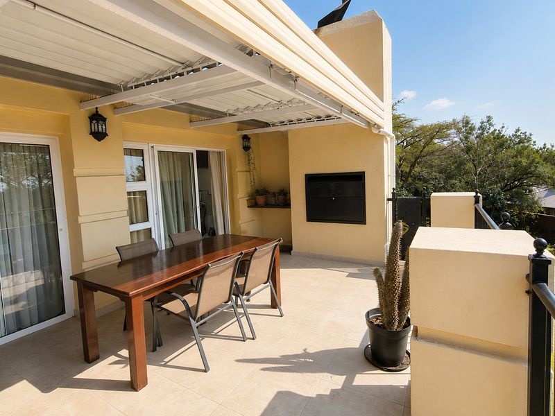 Spacious covered balcony featuring tiled flooring, a built-in braai, and sliding glass door access, offering a functional outdoor entertainment area.