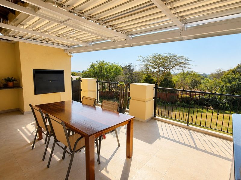 Spacious covered patio featuring a built-in braai, granite prep surface, and metal balustrade, offering pleasant views over the garden.