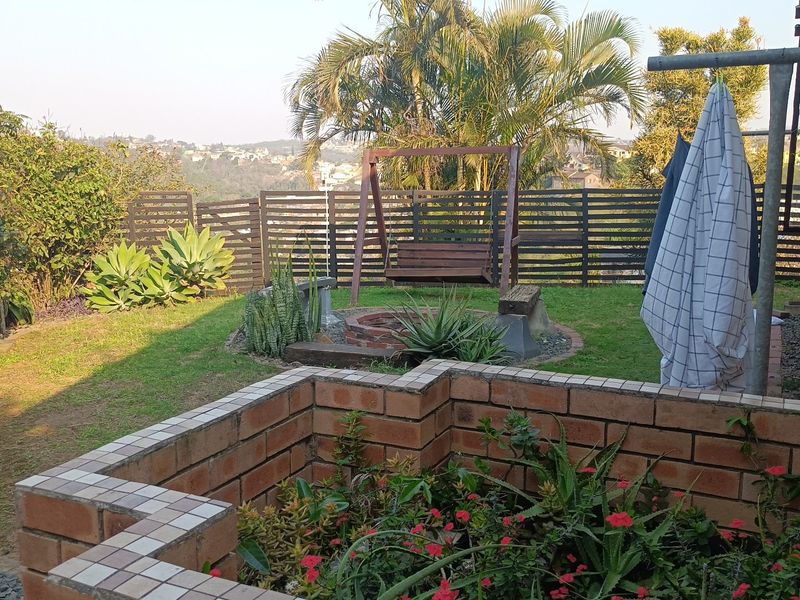A private rear garden featuring a brick planter box, a fire pit area, and timber slat fencing with scenic hillside views.