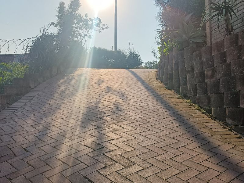 A paved driveway leading up to the property, featuring a tiered retaining wall and perimeter security fencing.