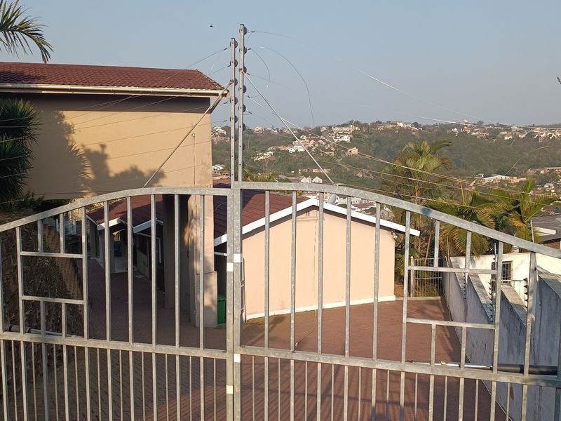 Front view of the property entrance featuring a metal security gate, electric fencing, and a paved driveway leading to the main building.