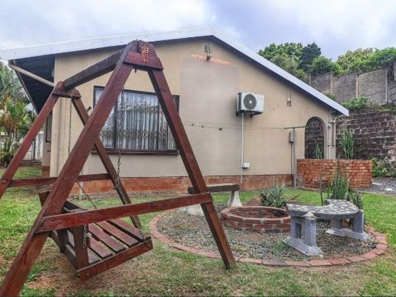 Rear garden area featuring a lawn, brick retaining wall, built-in barbecue, and exterior wall-mounted air conditioning unit.
