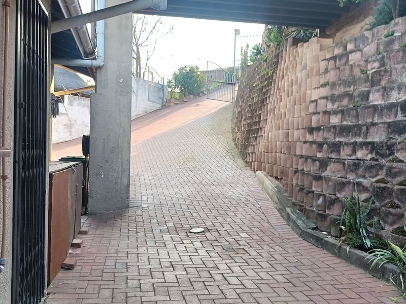 A paved driveway leading up a slope, featuring a substantial retaining wall and secure gated access to the property.