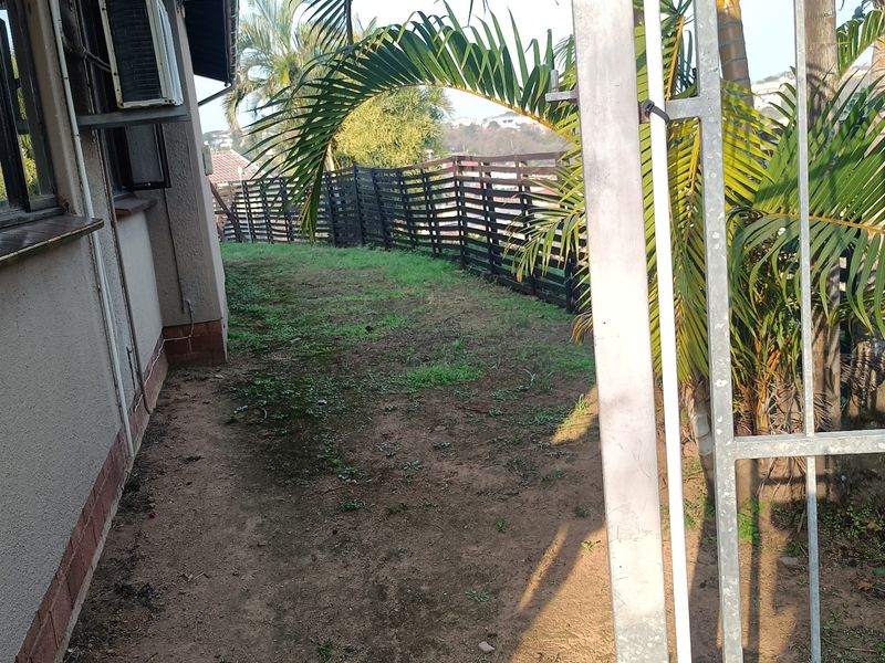 A side yard area featuring a metal security gate, timber fencing, and an external air conditioning unit mounted to the house wall.