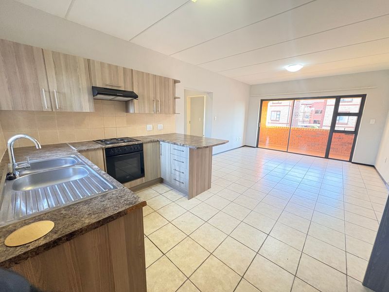 An open-plan kitchen and living area featuring tiled floors, built-in cabinetry with laminate countertops, and a sliding door leading to a balcony.