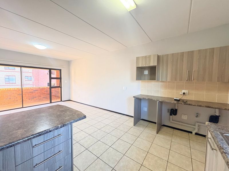 Open plan kitchen and living area featuring tiled flooring, modern laminate cabinetry, and a sliding door leading to a private balcony.