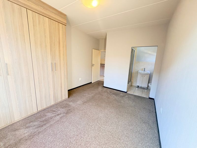 A spacious bedroom featuring neutral carpeting, a large built-in wardrobe, and an attached en-suite bathroom with a vanity and shower.