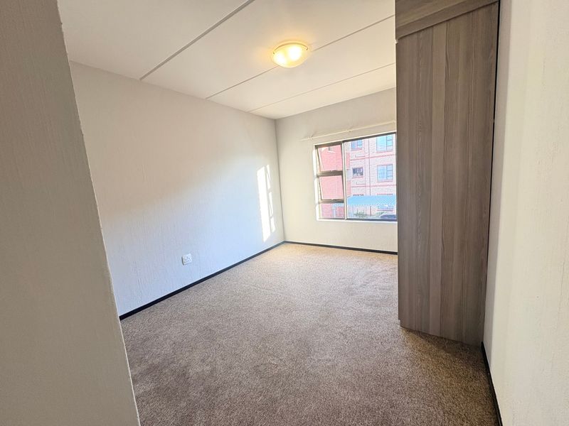 A clean, empty bedroom featuring neutral carpeting, a built-in wardrobe, and a window providing natural light.
