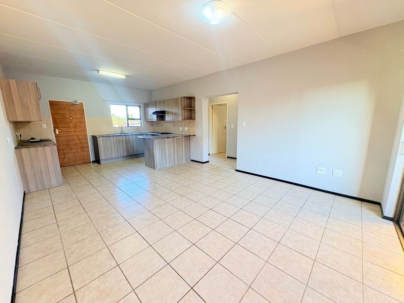 Spacious open-plan living area featuring tiled flooring and a functional kitchen with built-in cabinetry and laminate countertops.