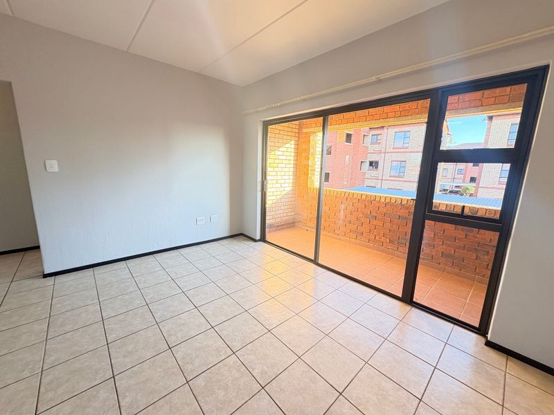 A bright, empty living area featuring neutral ceramic tile flooring and a large sliding glass door providing access to an outdoor balcony.