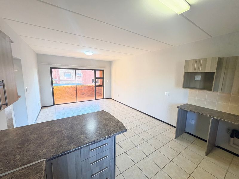 Open-plan living and kitchen area featuring tiled flooring, modern laminate cabinetry, and a sliding glass door leading to an outdoor balcony.