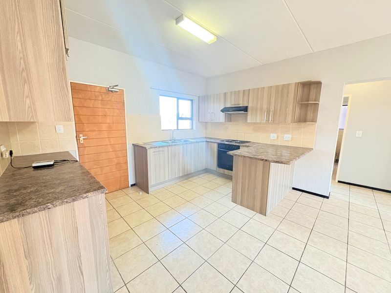 A functional kitchen featuring light wood-look cabinetry, laminate countertops, built-in oven with extractor fan, and neutral tiled flooring throughout.
