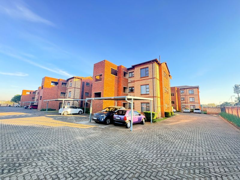Exterior view of a multi-story face brick apartment complex featuring paved parking areas and covered carports.