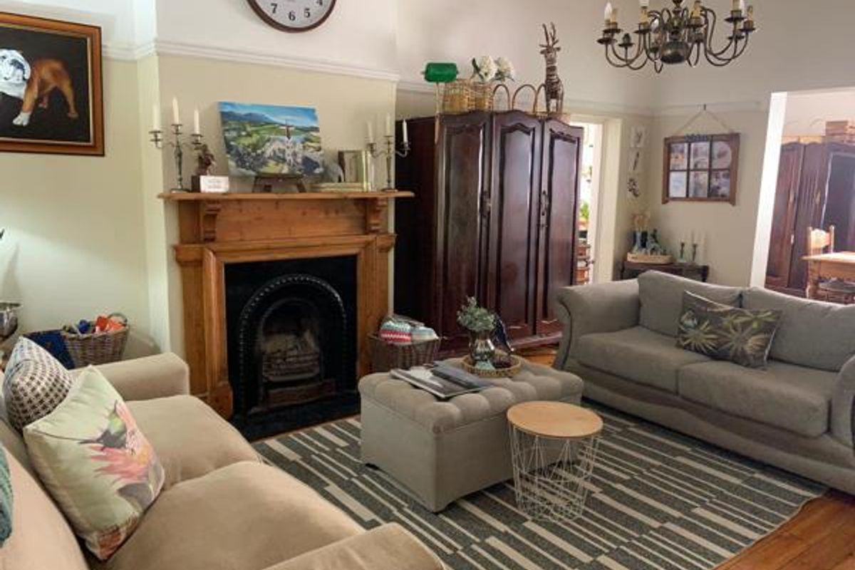 A cozy living room featuring a traditional timber fireplace mantel with a cast iron insert, complemented by polished timber flooring and classic ceiling detailing.