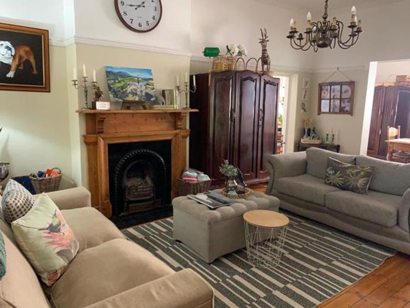 A cozy living room featuring a traditional timber fireplace mantel with a cast iron insert, complemented by polished timber flooring and classic ceiling detailing.
