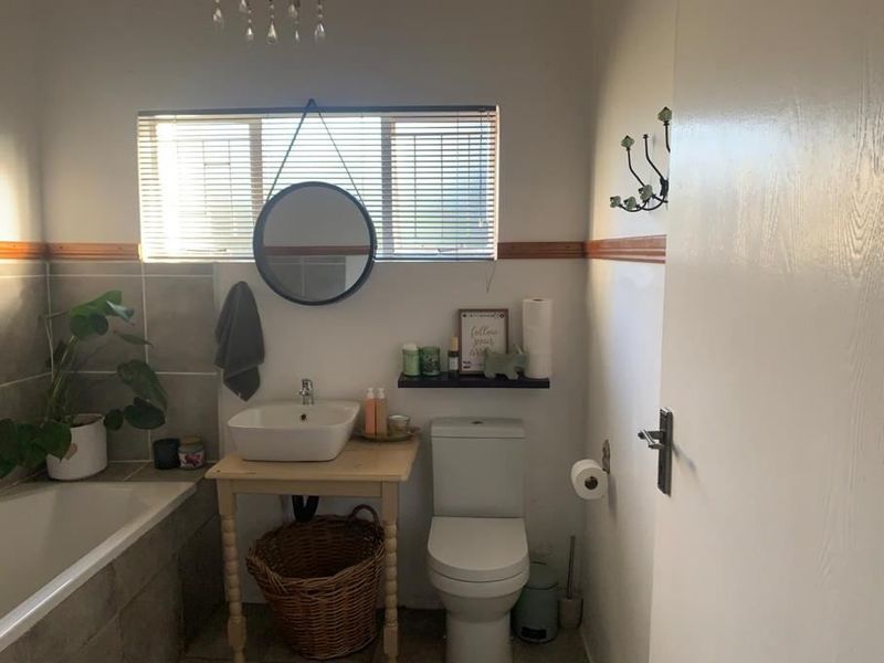 A functional bathroom featuring a built-in bathtub, tiled wall accents, a modern vessel sink, and a standard toilet with natural light from the window.