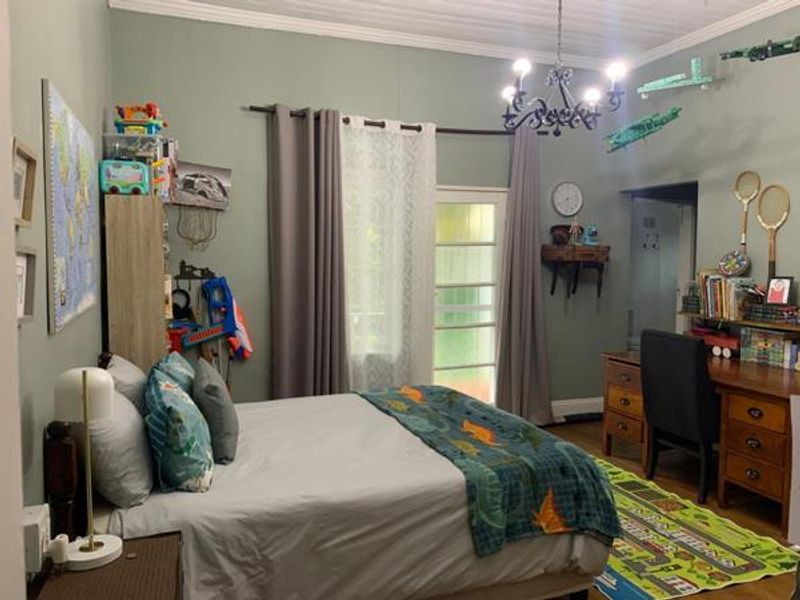 A well-maintained bedroom featuring crown molding, a classic chandelier, and a glass-paneled door providing natural light and access to the exterior.