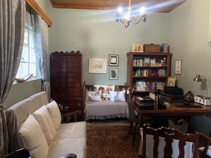 A cozy home office featuring a timber ceiling, classic chandelier, and ample natural light from the side window.
