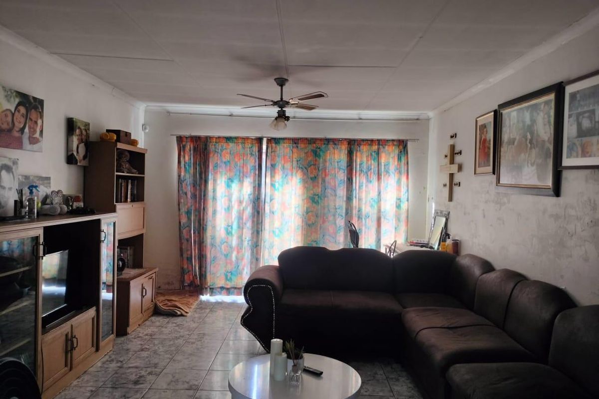 A living room featuring tiled flooring, a ceiling fan, and a sliding glass door leading to the exterior. The walls require cosmetic attention.