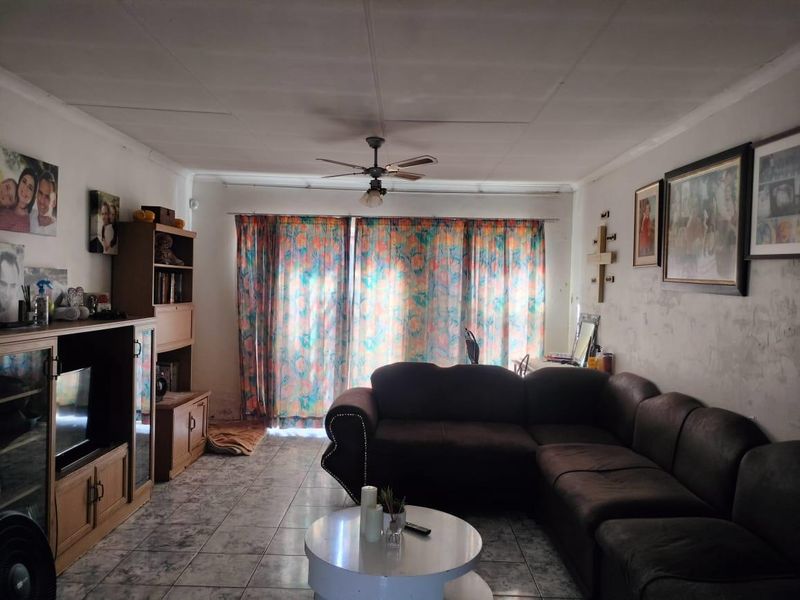 A living room featuring tiled flooring, a ceiling fan, and a sliding glass door leading to the exterior. The walls require cosmetic attention.