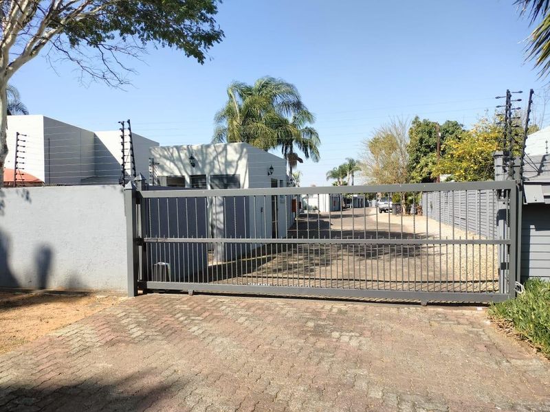 Front entrance view of the townhouse complex featuring a secure sliding gate, paved driveway, and perimeter wall with electric fencing.