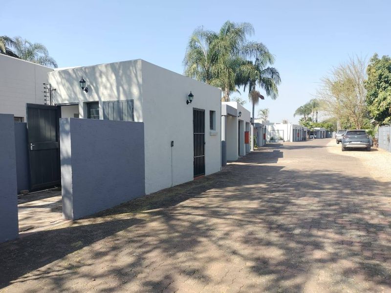 A view of the townhouse complex driveway featuring paved surfaces, boundary walls, and exterior security lighting along the residential units.